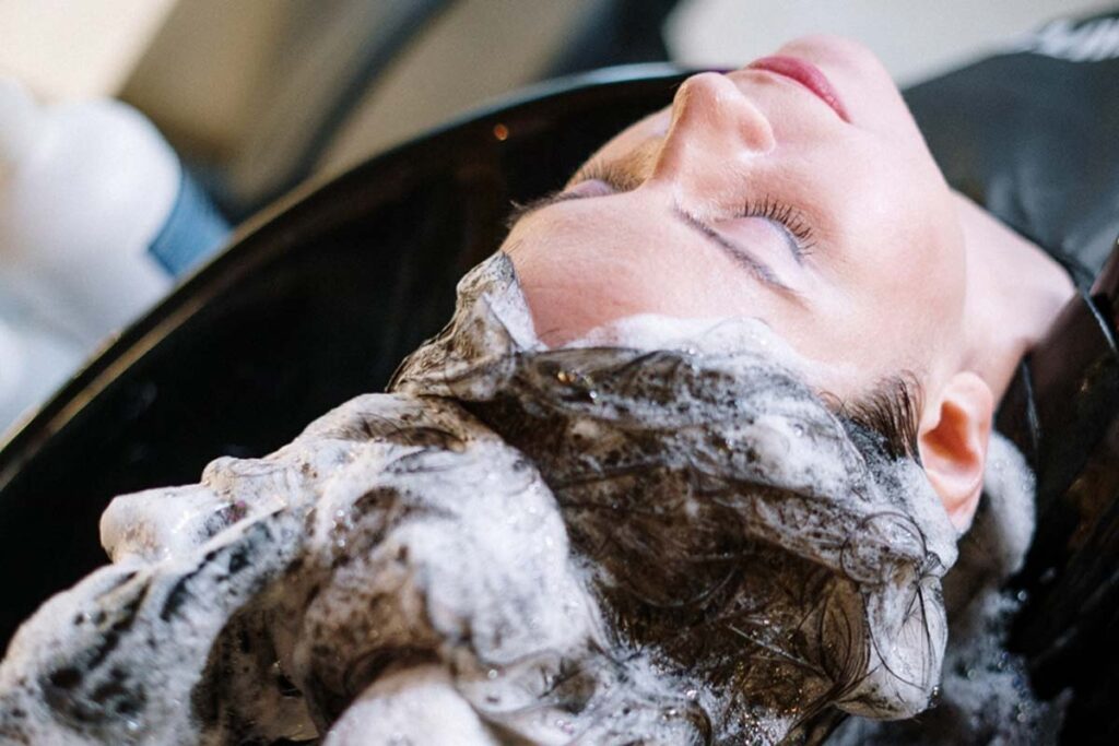 A woman having her hair washed in a salon sink, her hair covered in white shampoo lather.