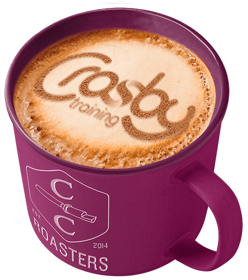 A purple coffee mug filled with a latte with the Crosby Training logo stencilled in the foam. 'C C Roasters' is printed on the side of the mug.
