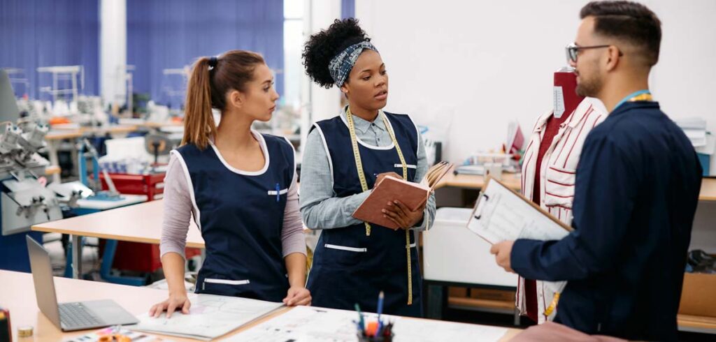 Three colleagues in a textiles factory are gathered around a desk with plans and a laptop.