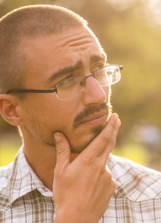 A young man rubs his chin and ponders thoughtfully.