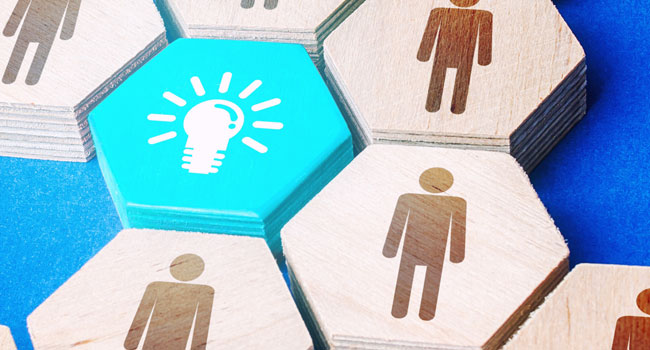 A set of wooden blocks with icons of people. One block is bright blue with a lightbulb symbol.