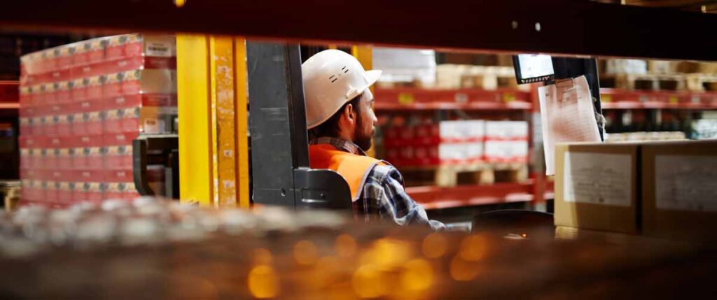 A warehouse employee operates a forklift in a large warehouse. 