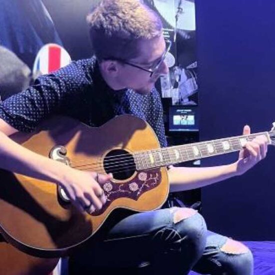 At a visit to the British Music Experience, young learner Richard sits cross legged with an acoustic guitar across his lap.