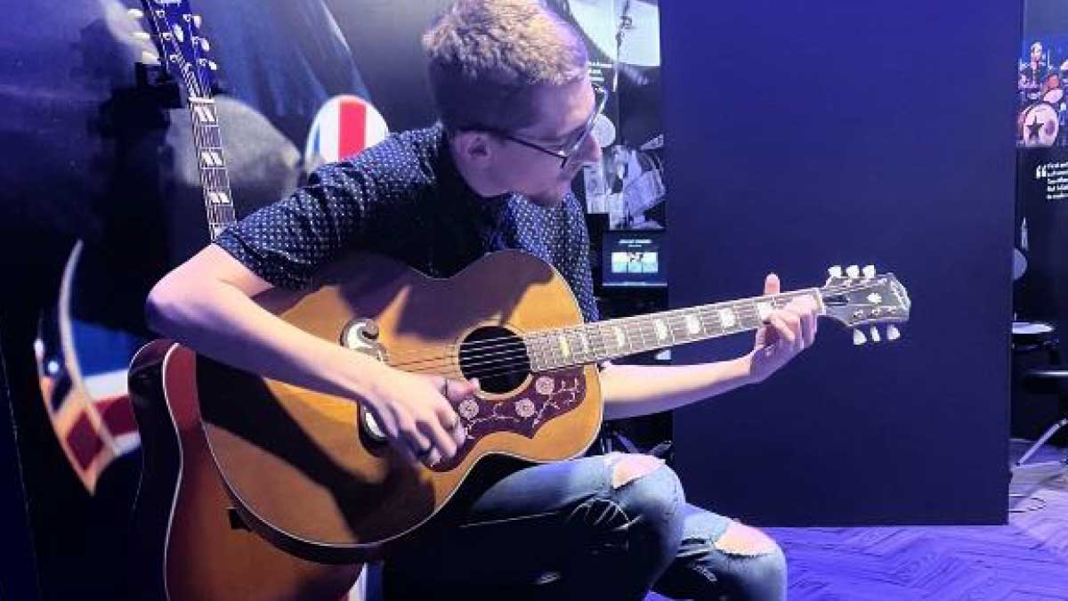 At a visit to the British Music Experience, young learner Richard sits cross legged with an acoustic guitar across his lap.