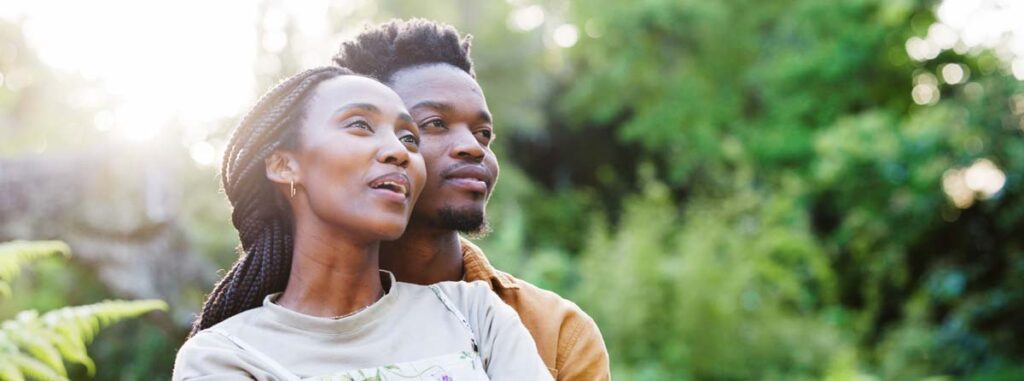 A young couple embrace in a softly light, vividly green park.