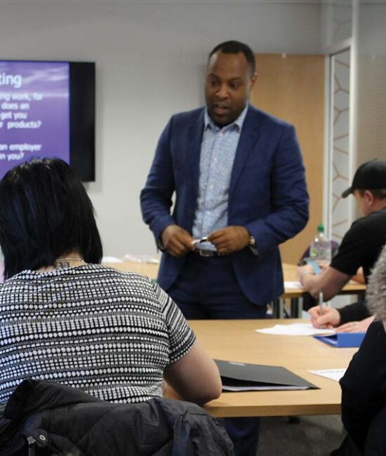 A guest presenter giving a talk to a group of Crosby Training learners. They appear to be listening intently. A man in the foreground is taking notes.