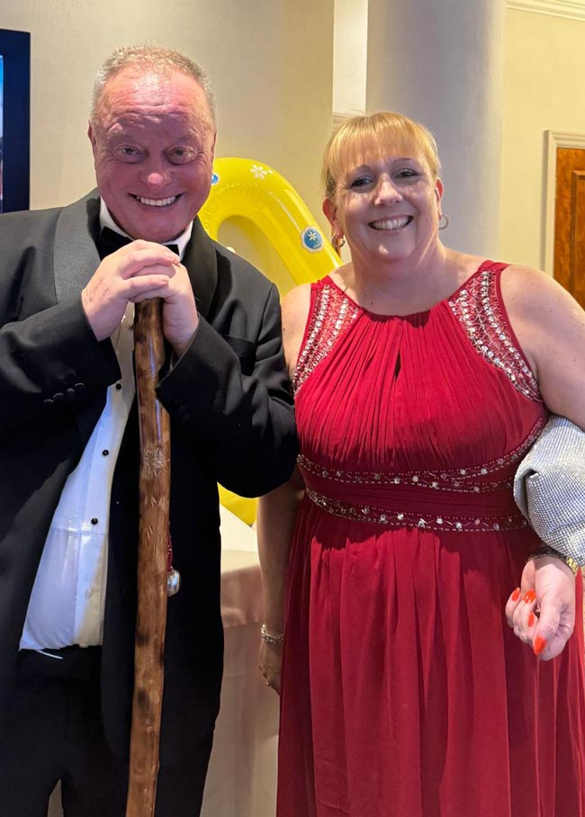 Dave Kelly of Daisy Inclusive UK and Crosby Training's Lisa Sumner looking very dapper in posh formal wear. He is wearing bow tie and dinner suit. She has a long flowing red dress.