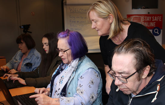 A Crosby Training tutor assisting four learners of various ages who are working on laptops.