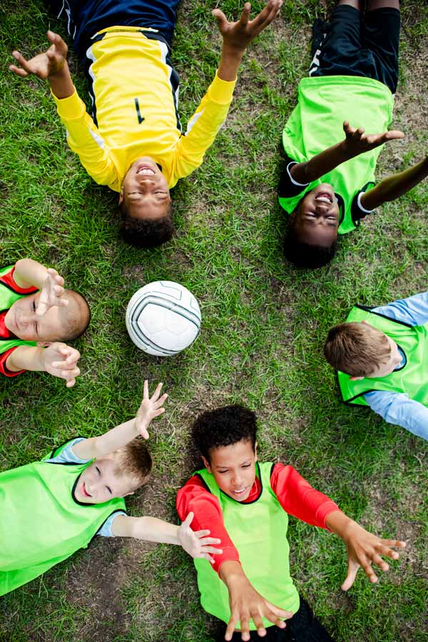 The group of children are lying on the pitch, arms stretched upwards.