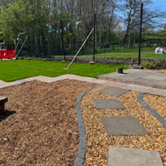 A light gravel path lined with paving bricks winds through a darker area of soil ready for planting. Trees in the distance create a boundary along a well cared for grassed area.