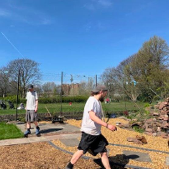 A bright spring day. Two learners in shorts working on the gravelled area they have created at Rice Lane farm.