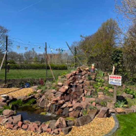 A large pile of carefully arranged rocks create a water feature. Small shrubs are planted amongst the rocks.