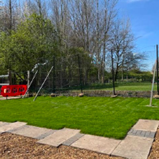 A lush grassed area with a fence on one side and a straight formal paved path on the other.