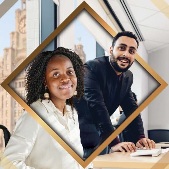A man and woman in business attire smile while sitting at a desk in an office with the Liver Building visible through the window.