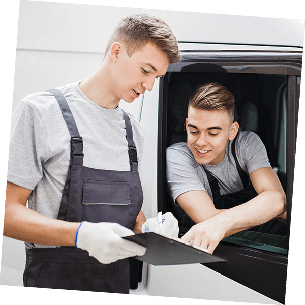 Two young men, one in a white van leaning out of the window pointing to a clipboard held by his colleague.