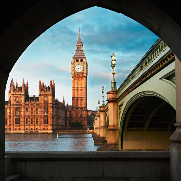 Big Ben and the Houses of Parliament framed by an archway of Westminster Bridge over the River Thames at sunrise.