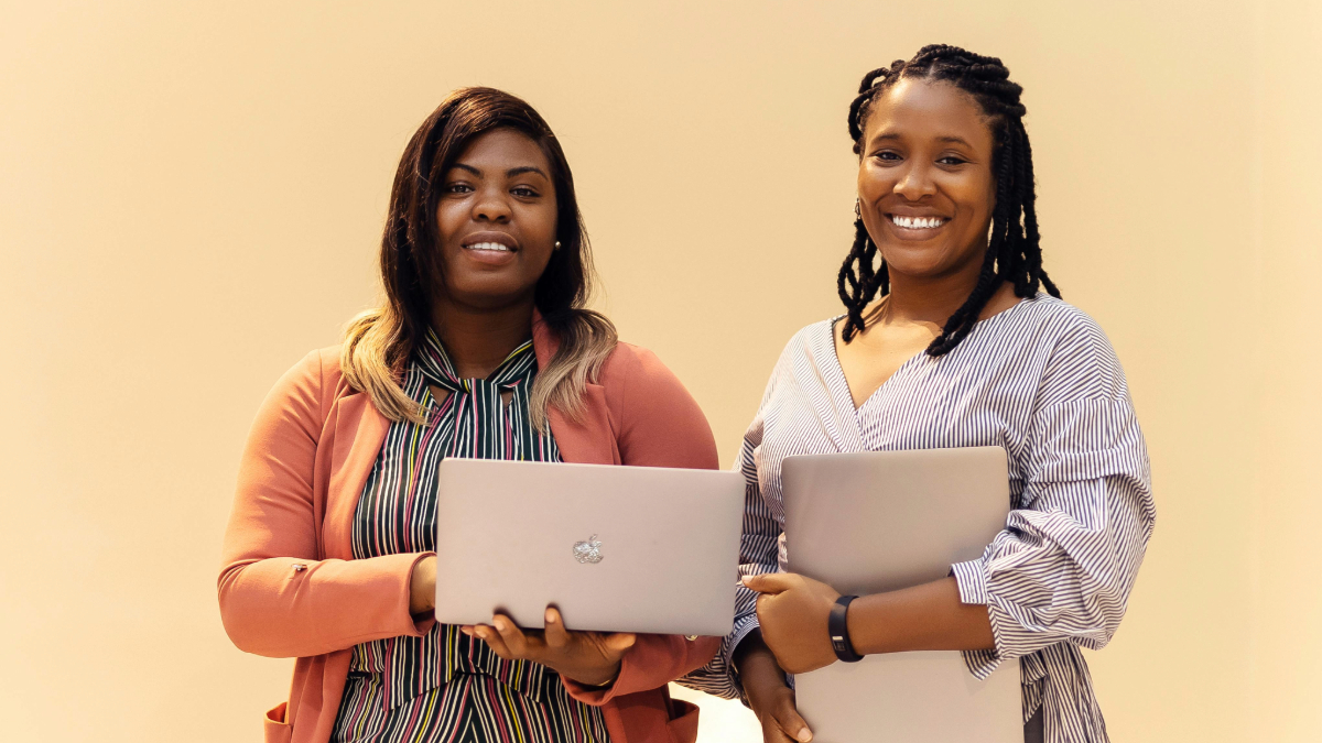 Learners smile holding laptops.